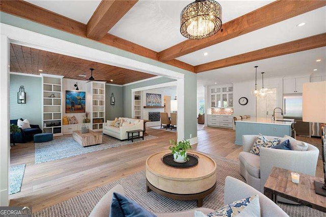 living room featuring sink, ceiling fan with notable chandelier, light hardwood / wood-style flooring, and beamed ceiling