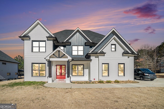 view of front facade featuring brick siding, roof with shingles, a front lawn, and french doors