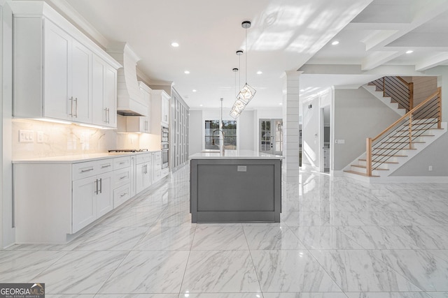 kitchen with custom range hood, light countertops, white cabinetry, and a center island with sink