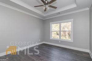 empty room with dark hardwood / wood-style floors, ceiling fan, ornamental molding, and a tray ceiling