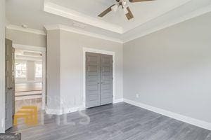 unfurnished bedroom with ceiling fan, ornamental molding, a tray ceiling, and dark hardwood / wood-style flooring