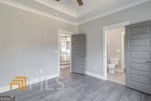 unfurnished bedroom with connected bathroom, dark wood-type flooring, ornamental molding, and a raised ceiling