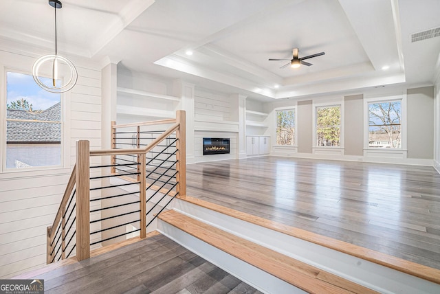 living room featuring dark wood-style flooring, visible vents, ornamental molding, a raised ceiling, and a glass covered fireplace