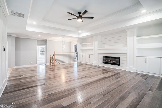 unfurnished living room with visible vents, a raised ceiling, dark wood-style floors, crown molding, and built in shelves