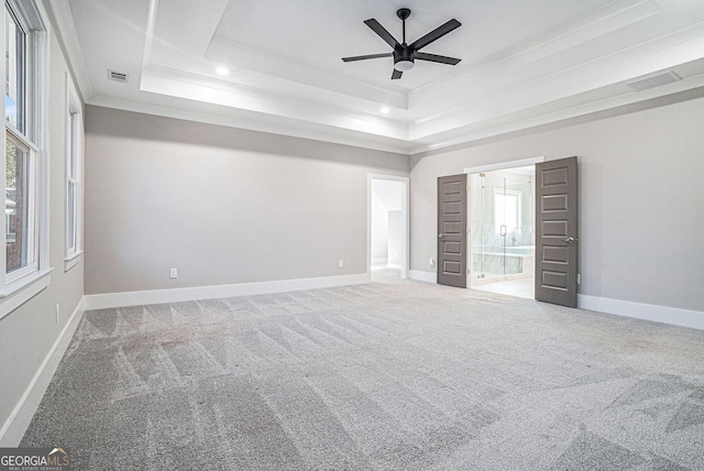 unfurnished bedroom featuring carpet floors, visible vents, baseboards, a tray ceiling, and crown molding