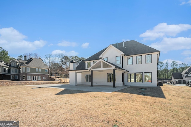 rear view of property featuring a patio area, a chimney, and a lawn