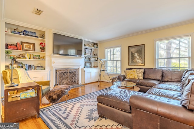 living room with built in features, ornamental molding, and light wood-type flooring