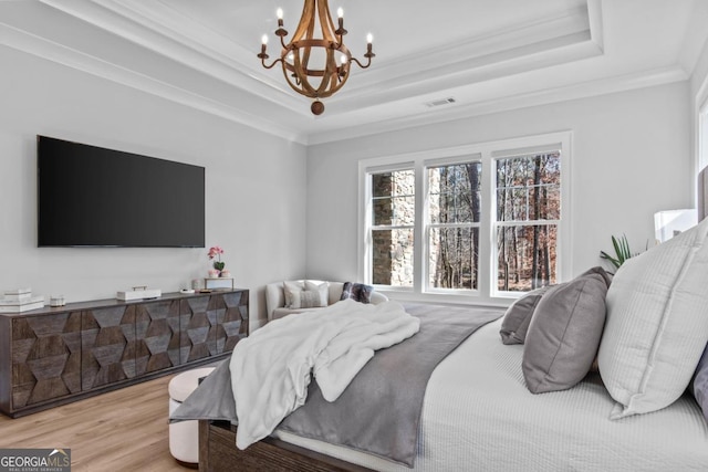 bedroom featuring a notable chandelier, a tray ceiling, ornamental molding, and light wood-type flooring