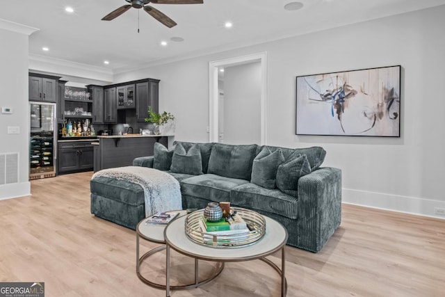 living room featuring ceiling fan, indoor bar, ornamental molding, and light hardwood / wood-style flooring