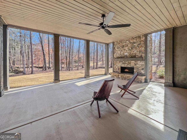 unfurnished sunroom featuring ceiling fan, wood ceiling, and an outdoor stone fireplace