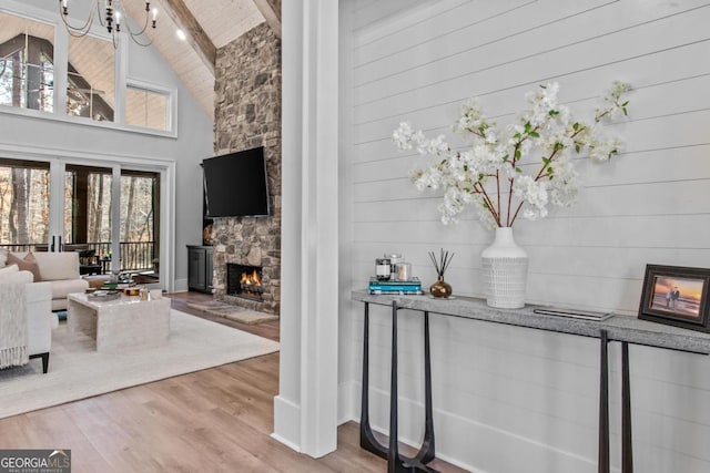 living room with hardwood / wood-style flooring, a stone fireplace, high vaulted ceiling, and beamed ceiling