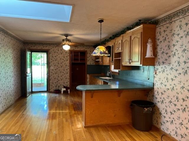 kitchen with a skylight, decorative light fixtures, sink, light hardwood / wood-style floors, and kitchen peninsula