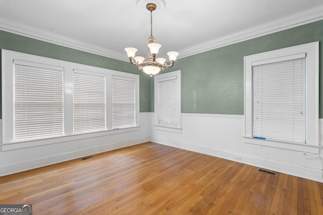 empty room with ornamental molding, wood-type flooring, and a notable chandelier