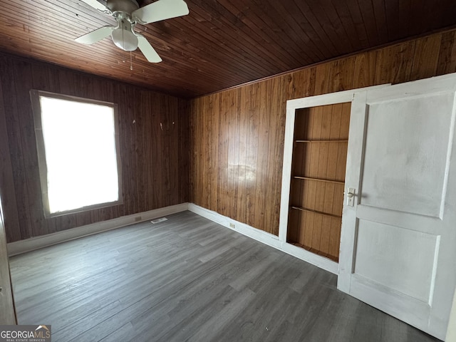 empty room with wooden walls, dark wood finished floors, wood ceiling, and baseboards