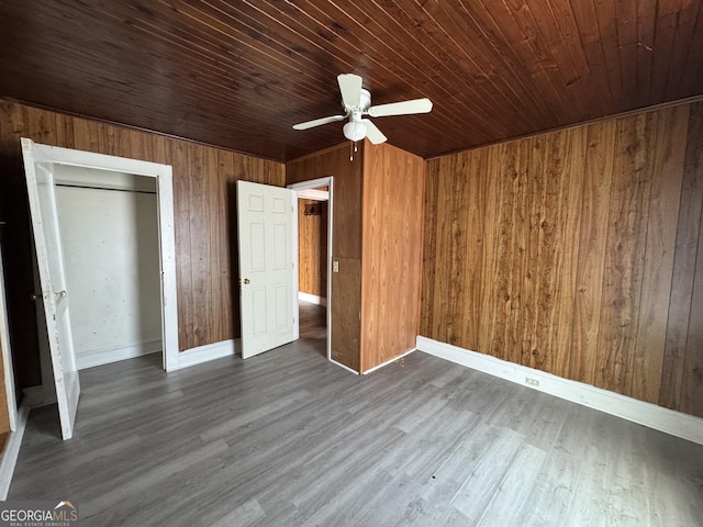 unfurnished bedroom featuring wooden ceiling, ceiling fan, dark wood-type flooring, wood walls, and a closet