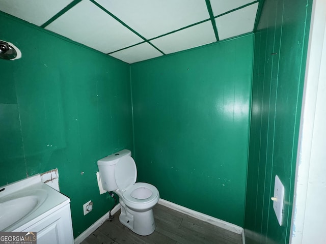 bathroom with a drop ceiling, toilet, wood finished floors, vanity, and baseboards