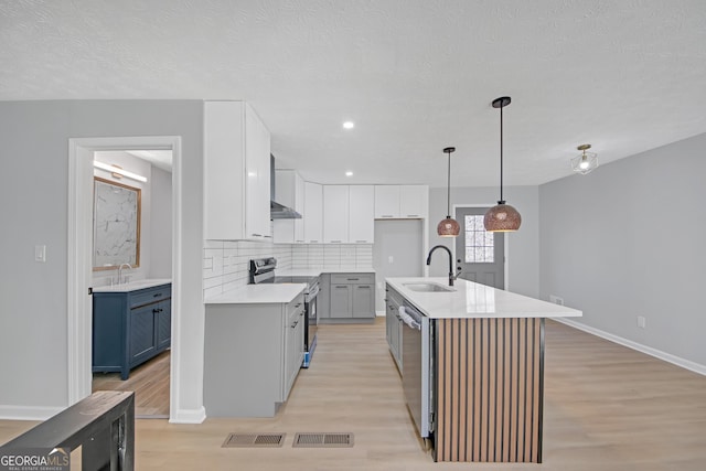 kitchen featuring sink, a center island with sink, pendant lighting, stainless steel appliances, and white cabinets