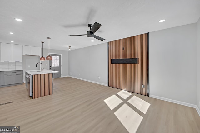 kitchen featuring light hardwood / wood-style flooring, gray cabinets, hanging light fixtures, backsplash, and an island with sink