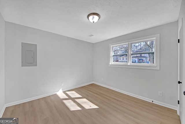 spare room featuring electric panel, light hardwood / wood-style floors, and a textured ceiling