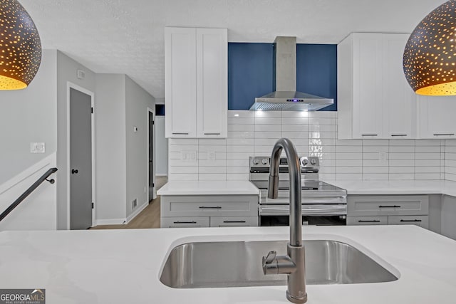 kitchen featuring white cabinetry, wall chimney range hood, stainless steel range with electric cooktop, and backsplash