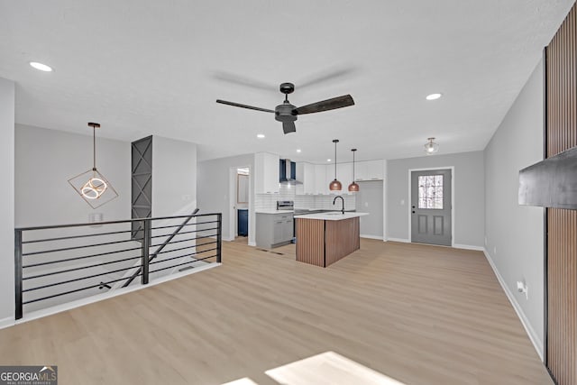 kitchen with wall chimney exhaust hood, a center island with sink, light wood-type flooring, pendant lighting, and decorative backsplash