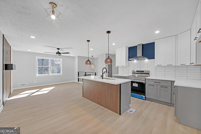 kitchen featuring wall chimney exhaust hood, sink, hanging light fixtures, an island with sink, and stainless steel electric stove