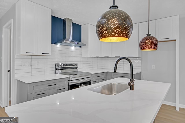 kitchen with sink, decorative light fixtures, electric range, light stone countertops, and wall chimney range hood