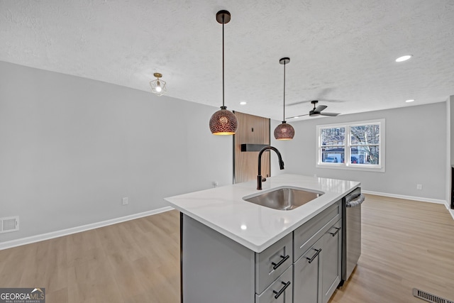 kitchen featuring pendant lighting, sink, light hardwood / wood-style flooring, dishwasher, and an island with sink