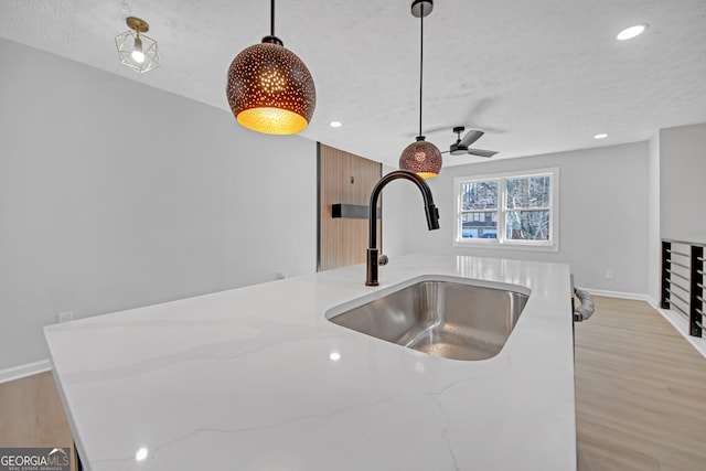 kitchen with sink, decorative light fixtures, light stone countertops, and light wood-type flooring