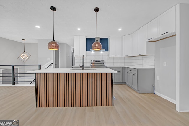 kitchen featuring sink, decorative light fixtures, stainless steel electric stove, and an island with sink