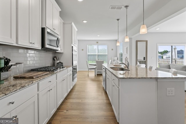 kitchen featuring white cabinetry, tasteful backsplash, pendant lighting, stainless steel appliances, and a kitchen island with sink