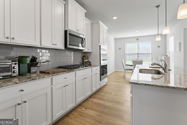 kitchen with pendant lighting, sink, stainless steel appliances, white cabinets, and decorative backsplash