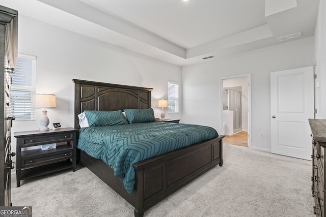 carpeted bedroom with multiple windows, a raised ceiling, and ensuite bathroom