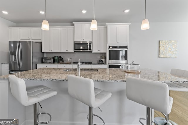 kitchen with stainless steel appliances, an island with sink, hanging light fixtures, and white cabinets