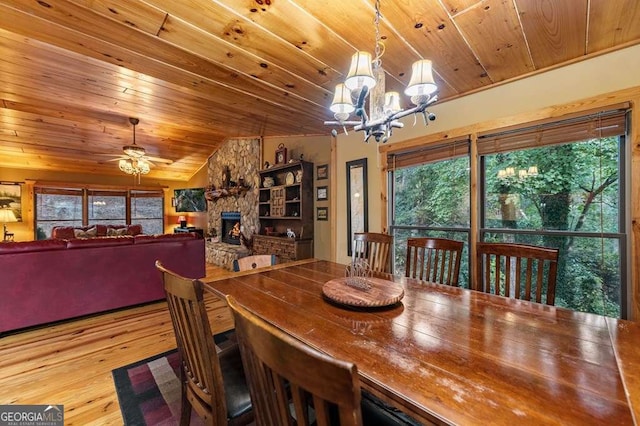 dining room featuring lofted ceiling, wood ceiling, a fireplace, light hardwood / wood-style floors, and ceiling fan with notable chandelier