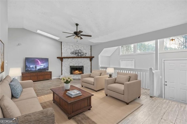 living room featuring vaulted ceiling, a textured ceiling, ceiling fan, a fireplace, and light hardwood / wood-style floors