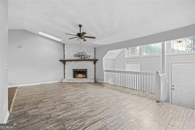 unfurnished living room featuring lofted ceiling, ceiling fan, a fireplace, light hardwood / wood-style floors, and a textured ceiling