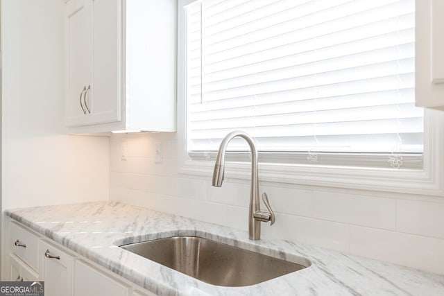 interior details with white cabinetry, sink, light stone counters, and backsplash