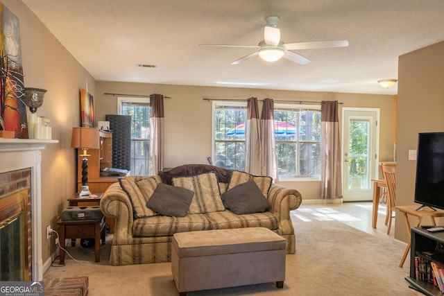 living room with ceiling fan, light colored carpet, a textured ceiling, and a fireplace