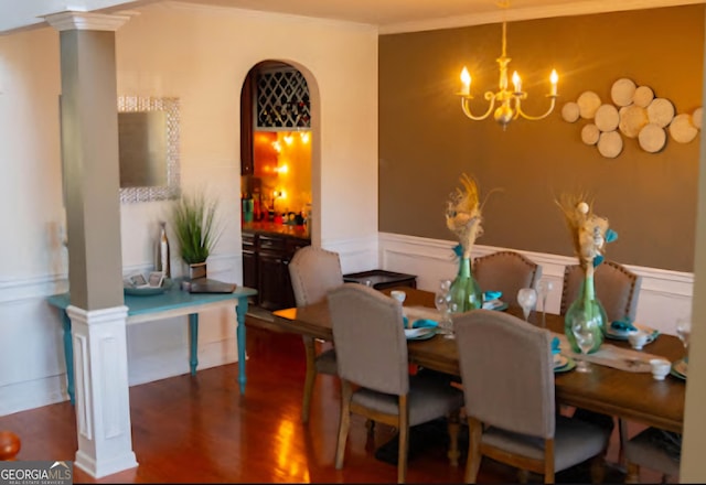 dining space featuring arched walkways, a wainscoted wall, wood finished floors, ornate columns, and a chandelier