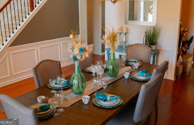 dining area featuring a decorative wall, wood finished floors, and wainscoting