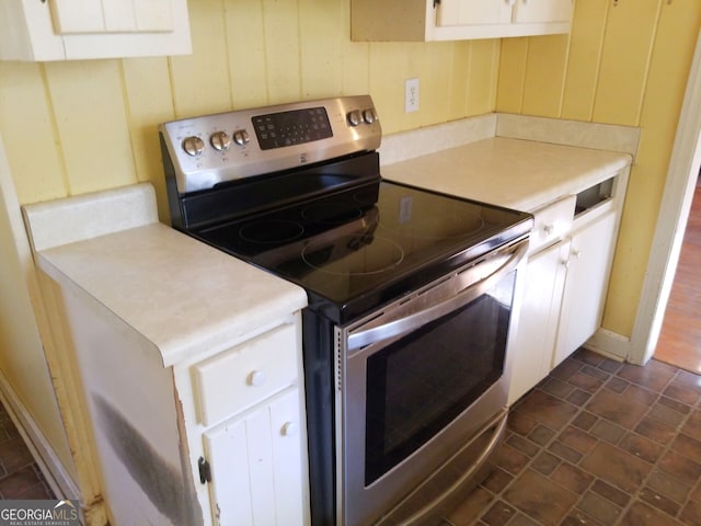 kitchen with white cabinets, wooden walls, and stainless steel electric range