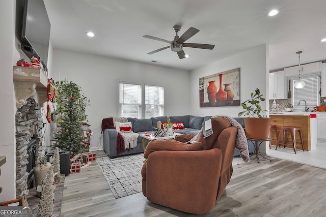 living room featuring ceiling fan, sink, and light wood-type flooring