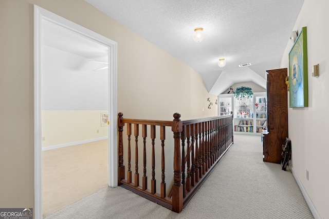 hall featuring light colored carpet, lofted ceiling, and a textured ceiling