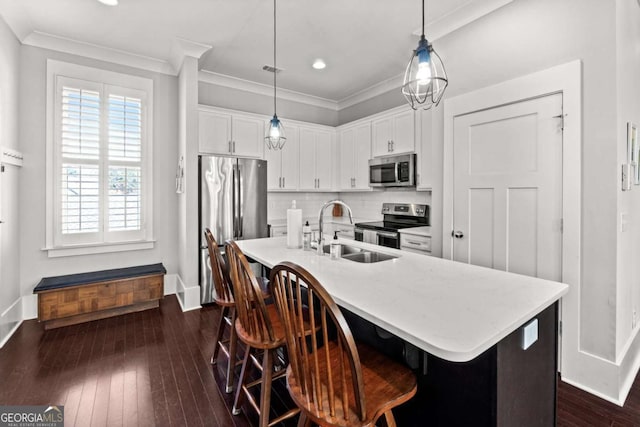 kitchen with pendant lighting, appliances with stainless steel finishes, sink, and a center island with sink