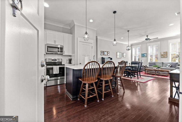 kitchen with appliances with stainless steel finishes, white cabinetry, a center island, a kitchen bar, and decorative light fixtures