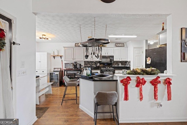 kitchen with a breakfast bar area, tasteful backsplash, white cabinets, hardwood / wood-style flooring, and black appliances