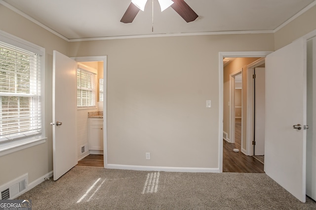 unfurnished bedroom with ornamental molding, ceiling fan, dark carpet, and ensuite bath