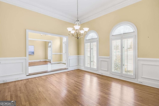 empty room with an inviting chandelier, crown molding, and wood-type flooring