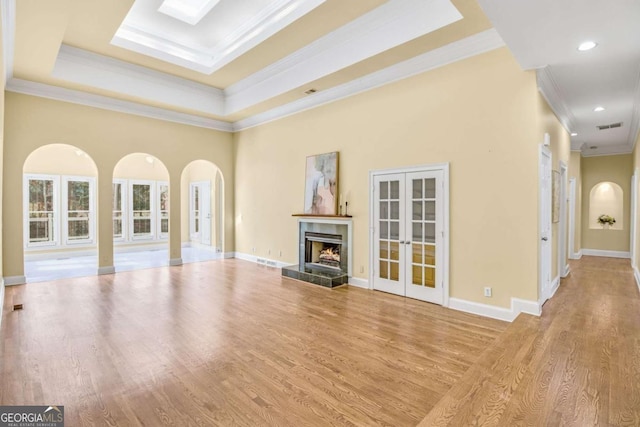 unfurnished living room with a towering ceiling, ornamental molding, light hardwood / wood-style floors, a tray ceiling, and french doors